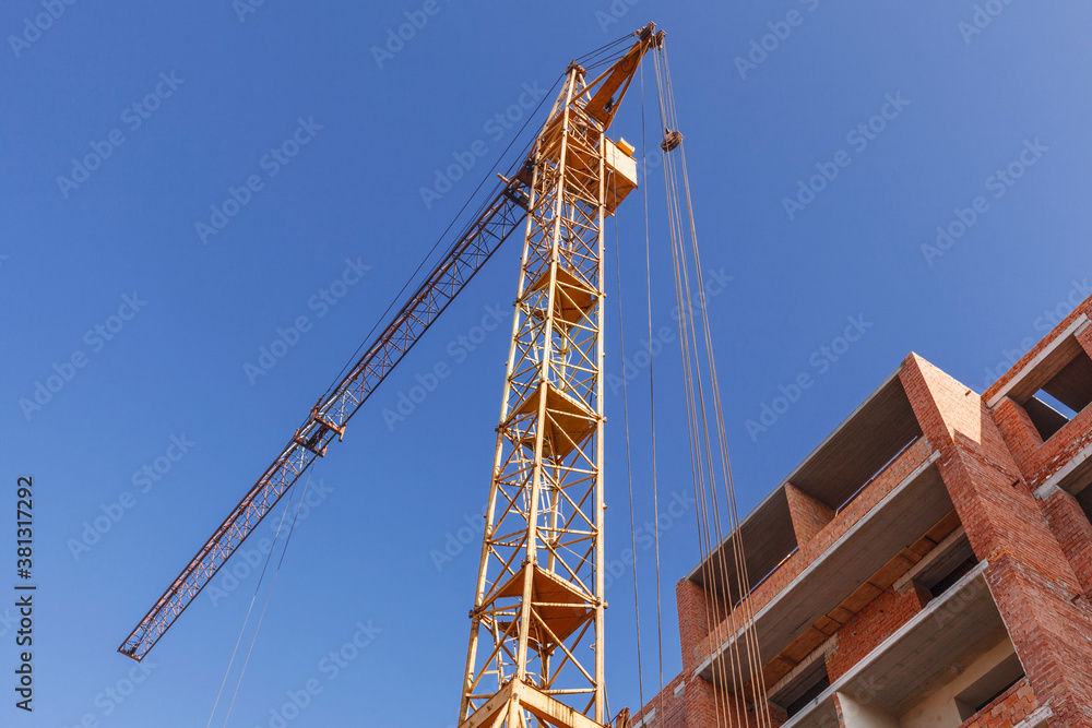 Tower crane near the building of a multi-storey house on a background of blue sky Tower crane near the building of a multi-storey house on a background of blue sky