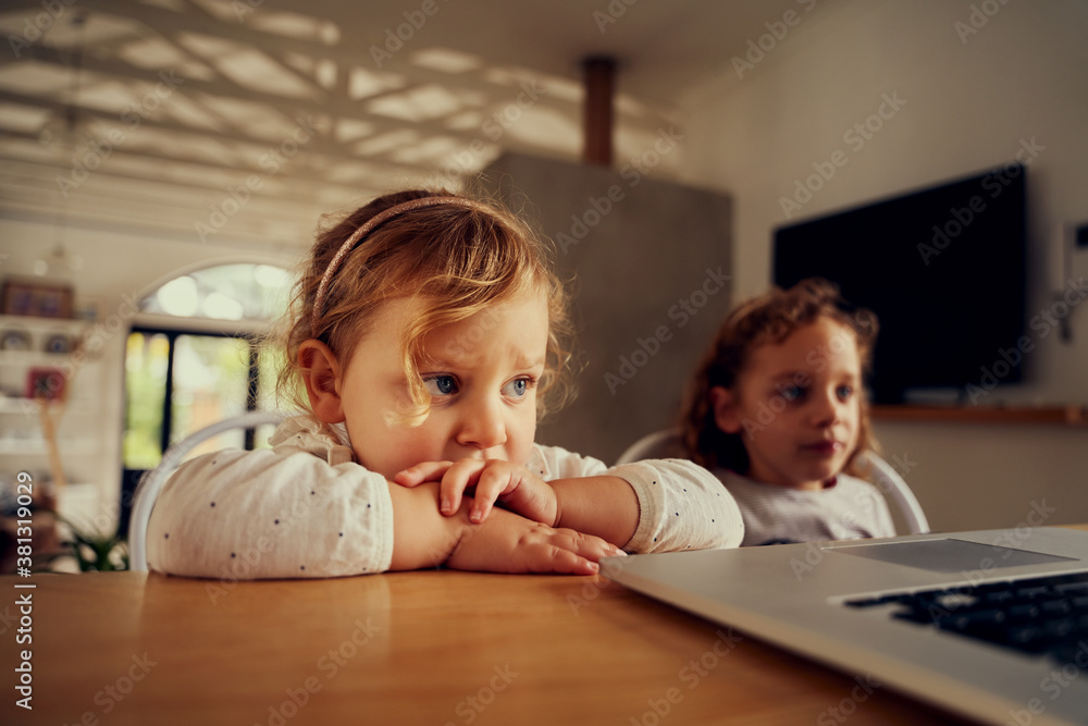 two young sisters watching a laptop in a modern home - two girls streaming on a laptop two young sisters watching a laptop in a modern home - two girls streaming on a laptop