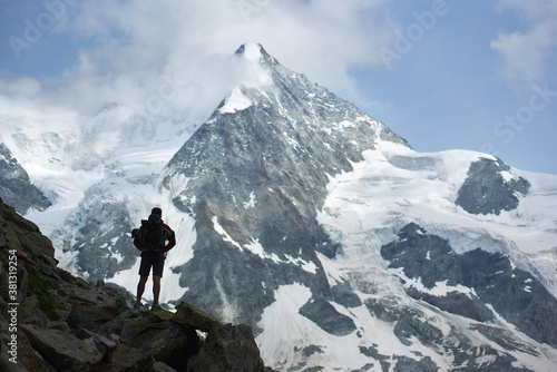 Horizontal snapshot of male tourist, standing with his back to the camera and enjoying the beauty of mount Ober Gabelhorn in Swiss Alps. Concept of travelling, tourism, hiking and alpinism