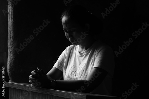 Slika na platnu Portrait of young woman kneeling and praying in silent prayer pose, on black and white background