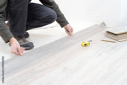 DIY, repair, building and home concept - close up of male hands lying parquet floor board/laminate flooring