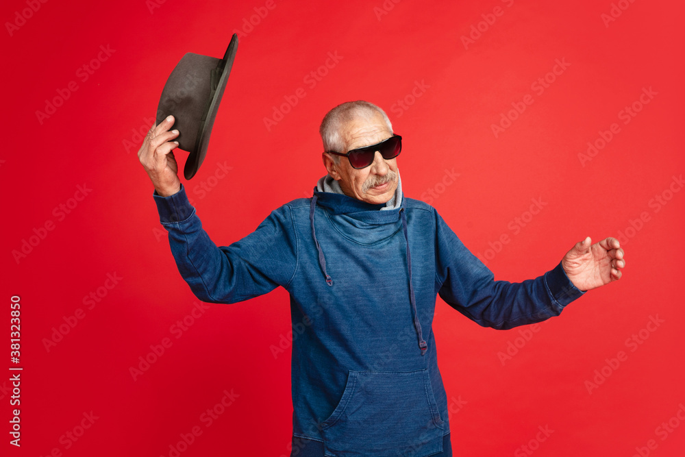 Greeting. Portrait of senior man in stylish eyewear and hat isolated on red studio background. Tech and joyful elderly lifestyle concept. Trendy colors, forever youth. Copyspace for your ad. Greeting. Portrait of senior man in stylish eyewear and hat isolated on red studio background. Tech and joyful elderly lifestyle concept. Trendy colors, forever youth. Copyspace for your ad.