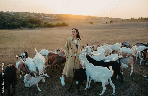 Tablou pe pânză Shepherdess stands in a pasture among goats at sunset.