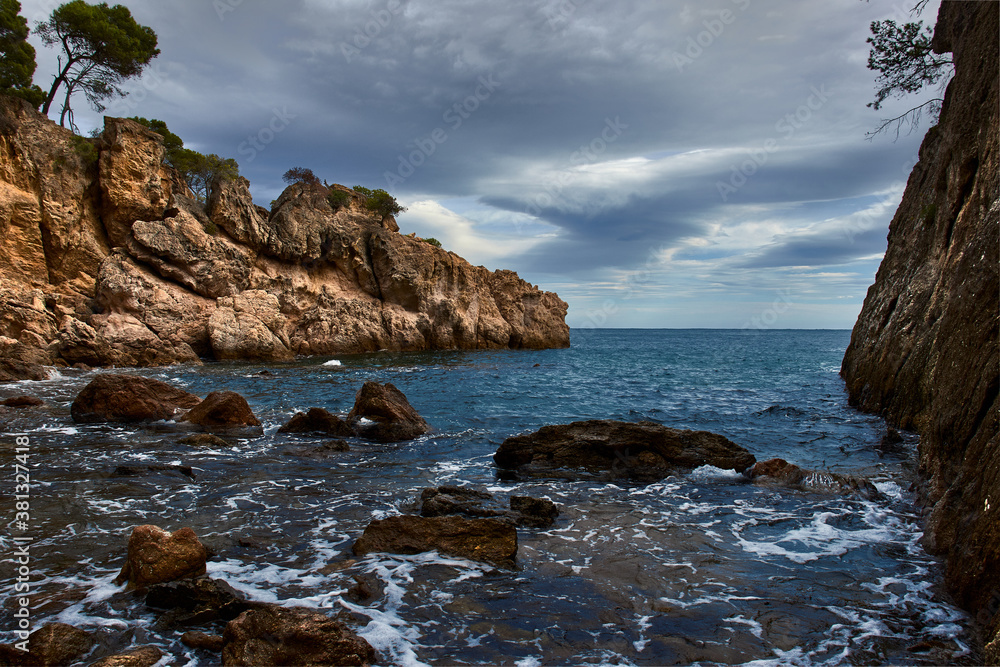 Seascape, with a rocky coast that juts out into the sea, under a sky covered with gray clouds
