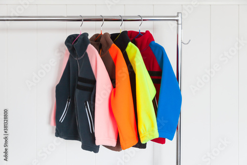 Colorful fleece jackets are on a rack near wall photo