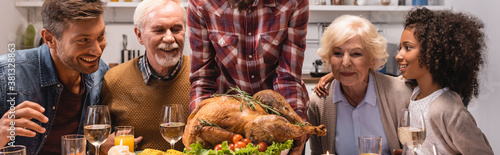 Panoramic crop of woman holding turkey while celebrating thanksgiving with multiethnic family