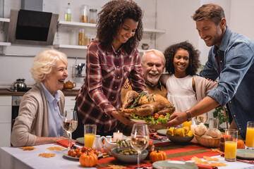 Selective focus of multiethnic family standing near turkey and thanksgiving dinner at home