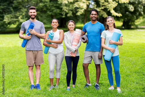 fitness, sport and healthy lifestyle concept - group of happy people with yoga mats at park