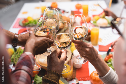 partial view of multiethnic relatives clinking wine glasses while celebrating thanksgiving day