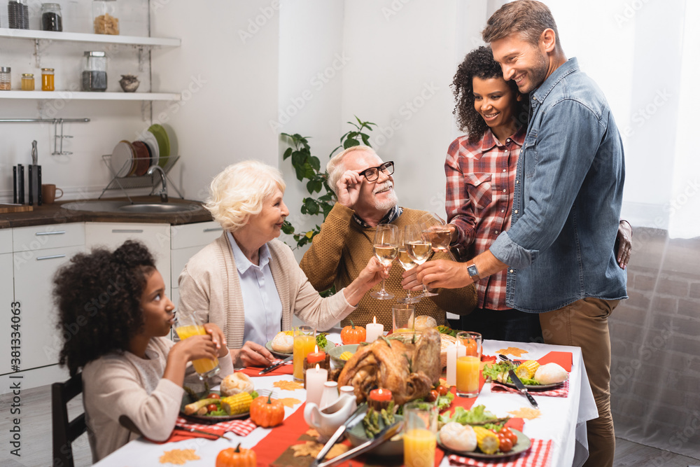 excited multiethnic family clinking wine glasses while celebrating thanksgiving day