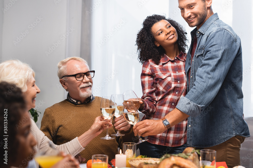 selective focus of multicultural family clinking glasses of white wine while celebrating thanksgiving day selective focus of multicultural family clinking glasses of white wine while celebrating thanksgiving day