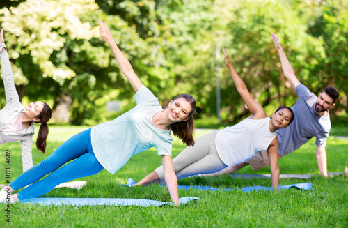 fitness, sport and healthy lifestyle concept - group of happy people doing yoga at summer park