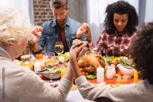 selective focus of multiethnic family with closed eyes holding hands on thanksgiving holiday