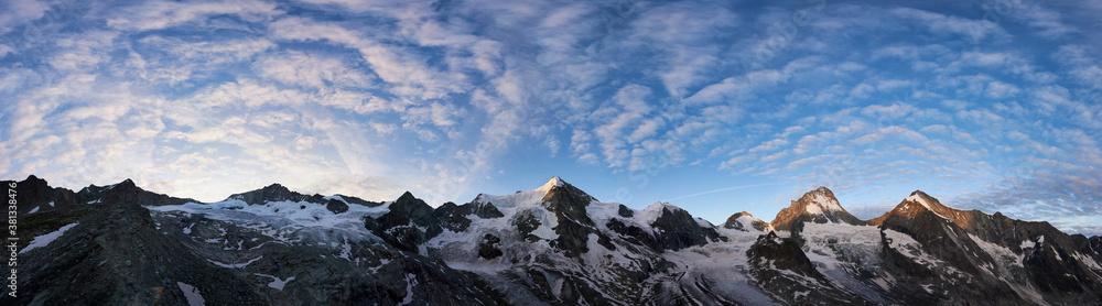 Panoramic snapshot of a ridge of rocky mountains in Switzerland in the morning, blue sky with wavy clouds is over snowy peaks, rising sun shining at Ober Gabelhorn and Dent Blanche
