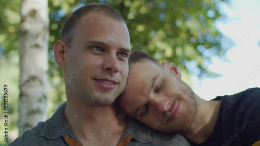 Portrait of handsome gay man with eyes closed leaning head on beloved boyfriend's shoulder, talking and bonding while affectionate homosexual couple enjoying leisure together in summer nature. Portrait of handsome gay man with eyes closed leaning head on beloved boyfriend's shoulder, talking and bonding while affectionate homosexual couple enjoying leisure together in summer nature.
