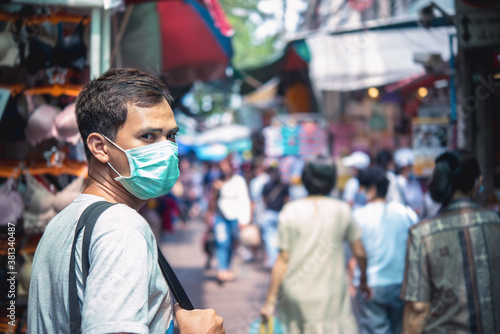 Young handsome man walking around market in Thailand with backpack and wearing a face pollution mask to protect himself from the coronavirus.