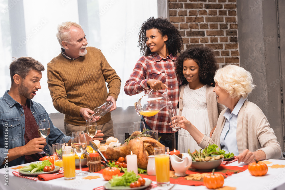 joyful african american man and senior woman looking at each other while pouring beverages during thanksgiving dinner joyful african american man and senior woman looking at each other while pouring beverages during thanksgiving dinner