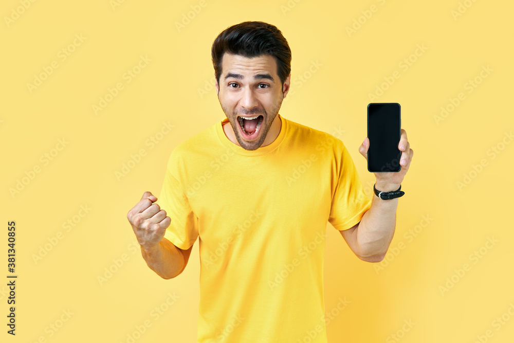Excited screaming man holding mobile phone and looking to camera in yellow studio Excited screaming man holding mobile phone and looking to camera in yellow studio
