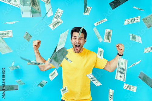 Happy excited man standing under money rain banknotes falling down