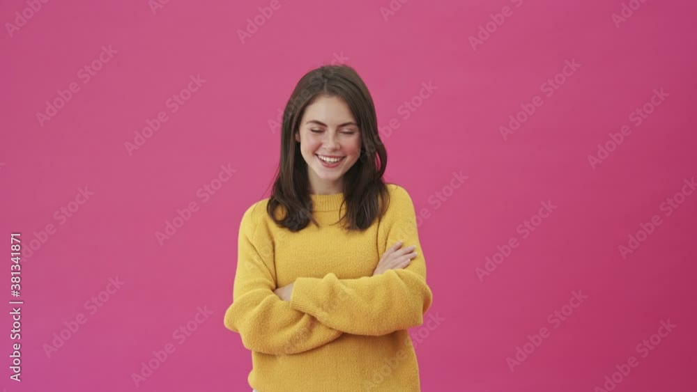 A smiling woman in a yellow sweater is standing isolated over a pink background A smiling woman in a yellow sweater is standing isolated over a pink background