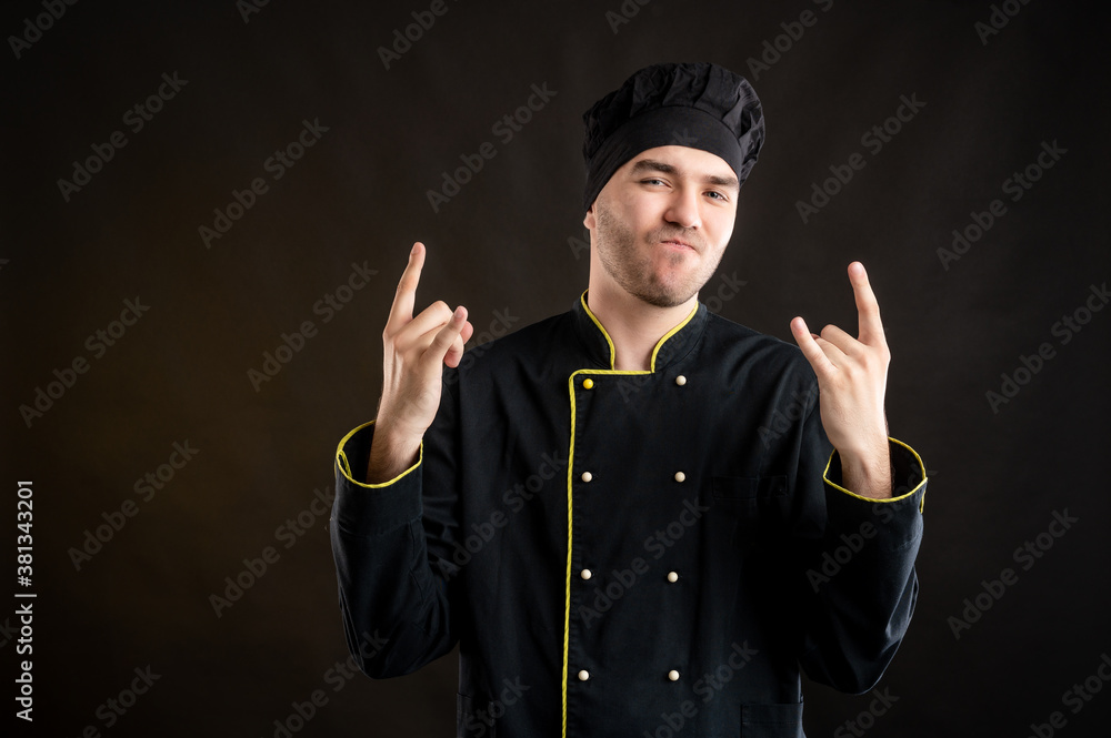 Young male dressed in a black chef suit doing rock symbol with hands up Young male dressed in a black chef suit doing rock symbol with hands up