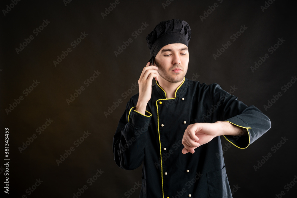 Young male dressed in a black chef suit showing it's time gesture Young male dressed in a black chef suit showing it's time gesture