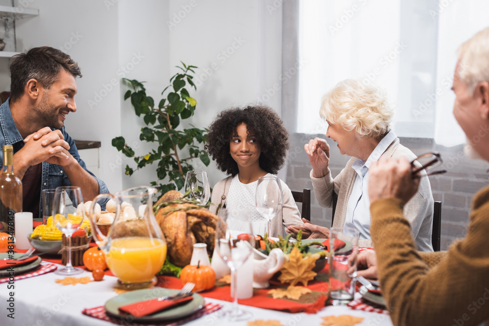 selective focus of senior woman talking to african american granddaughter during thanksgiving dinner