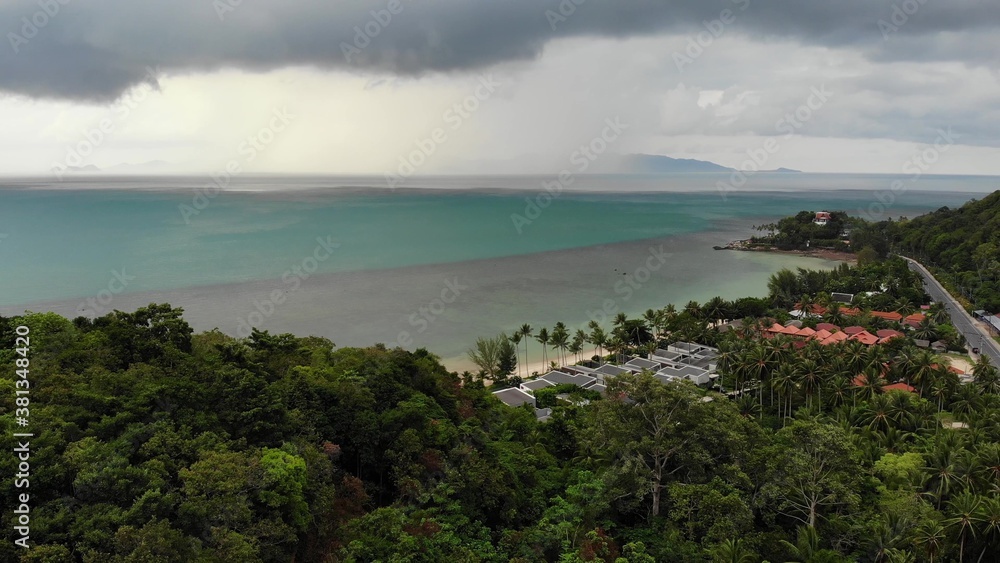 Overcast sky over tropical island. Gray cloudy sky, green palms on Koh Samui during wet season in Thailand. Drone view. Flying over wild rainforest and jungle near paradise ocean beach. Storm in Asia