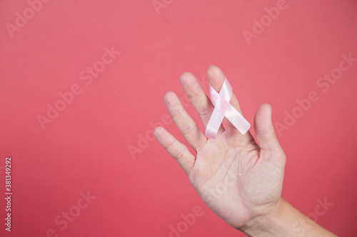 Pink ribbon in a woman hands on pink background.