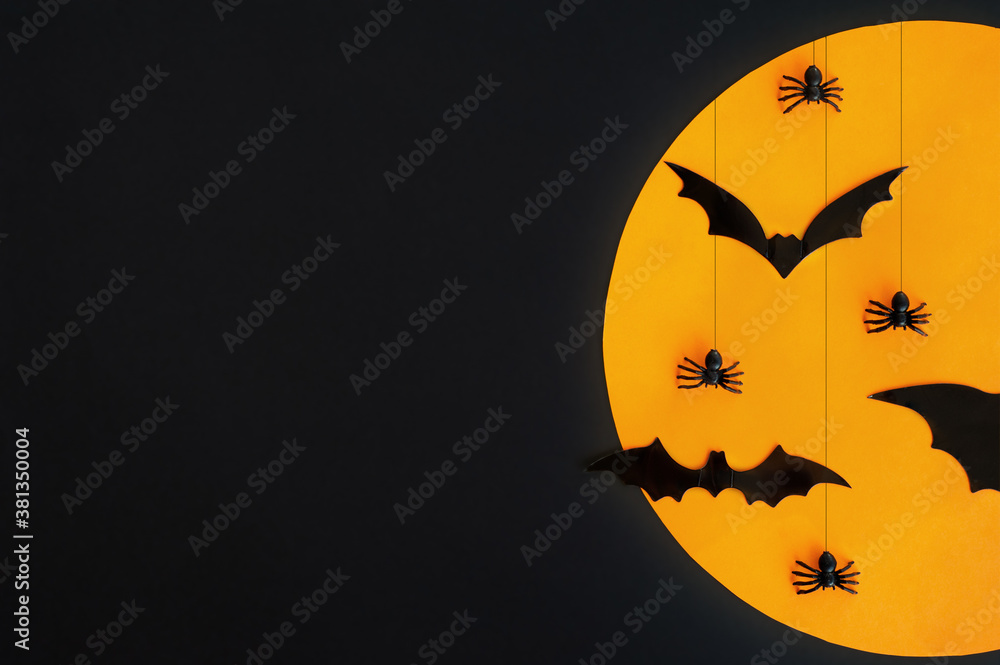 Halloween. Composition. Black bats and spiders against the orange moon and black background. Copy space.