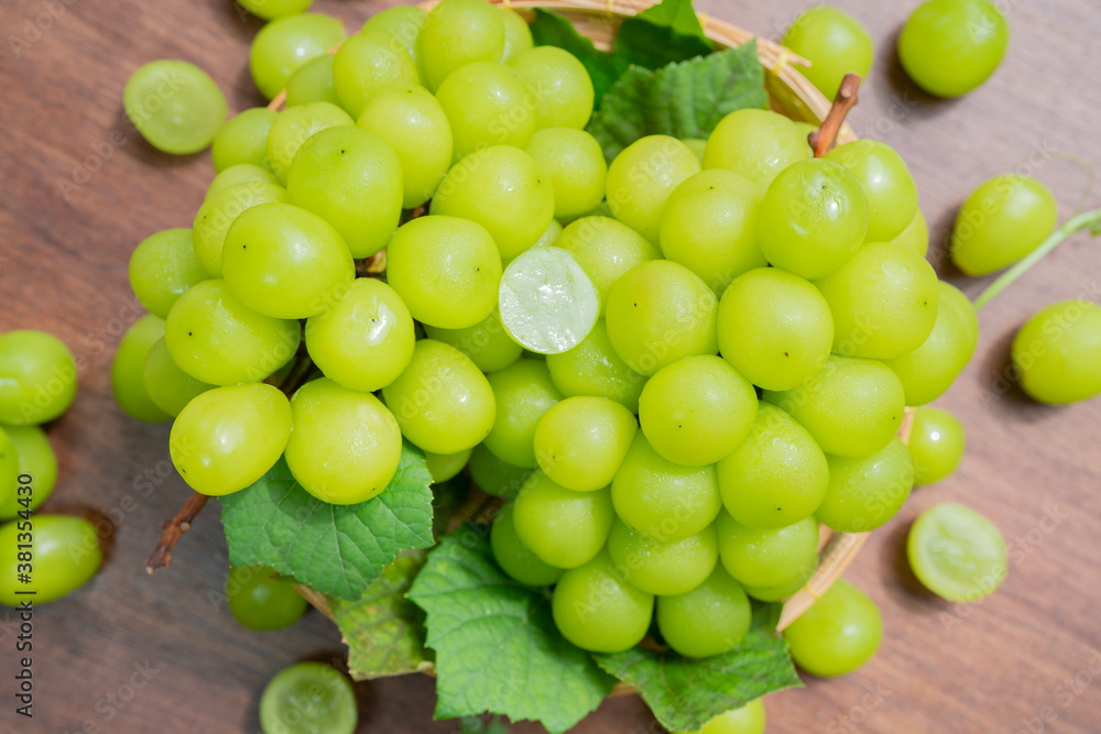 Green grape in Bamboo basket on wooden table in garden, Shine Muscat Grape with leaves in wooden background Green grape in Bamboo basket on wooden table in garden, Shine Muscat Grape with leaves in wooden background