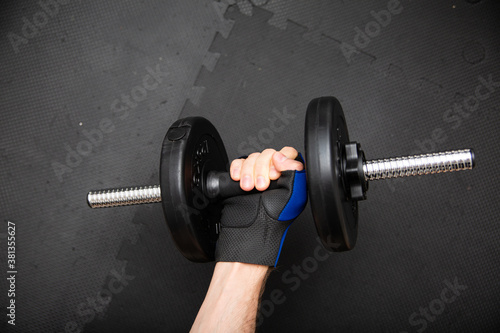 Male hand in a gym glove, holding a dumbbell, top view.