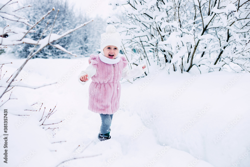 .A little girl in a pink fur coat stands in the middle of a snow-covered park