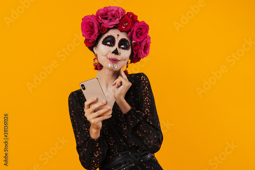 Photo of girl in halloween makeup and flower wreath using mobile phone