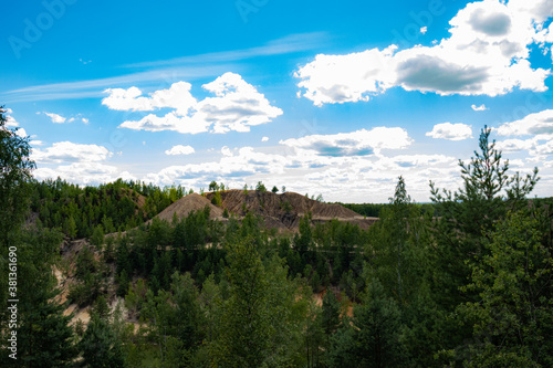 Reclaimed abandoned sand and clay quarry. Many trees have grown on the sandy slopes. Beautiful sunny summer landscape.