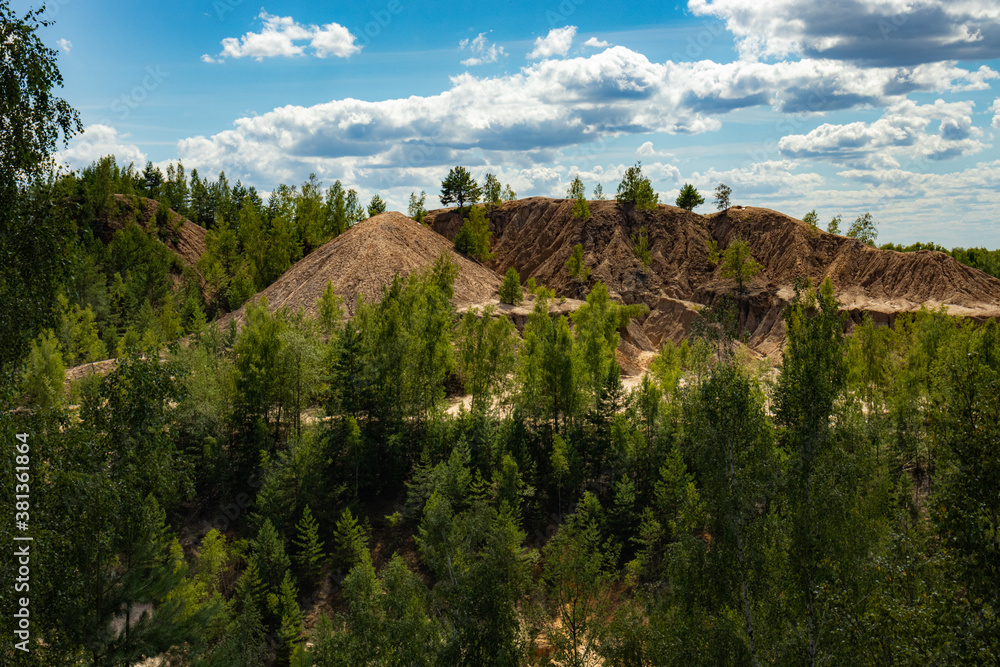 Reclaimed abandoned sand and clay quarry. Many trees have grown on the sandy slopes. Beautiful sunny summer landscape. Reclaimed abandoned sand and clay quarry. Many trees have grown on the sandy slopes. Beautiful sunny summer landscape.