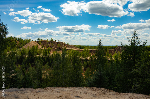 Reclaimed abandoned sand and clay quarry. Many trees have grown on the sandy slopes. Beautiful sunny summer landscape.