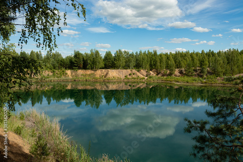 Reclaimed abandoned sand and clay quarry. A large lake with clear blue water has formed in its center, trees have grown.