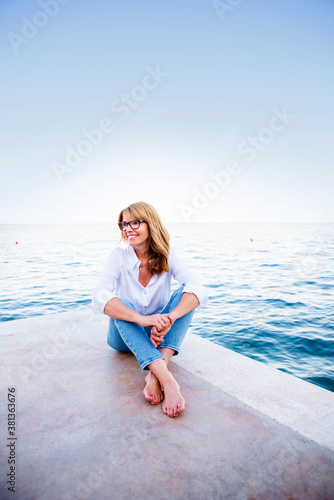Beautiful mature woman sitting on cliff and relaxing by the sea