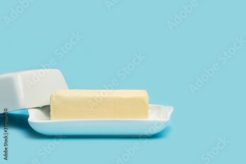 Mantequilla entera dentro de una mantequera blanca sobre un fondo celeste pastel liso y aislado. Vista de frente. Copy space