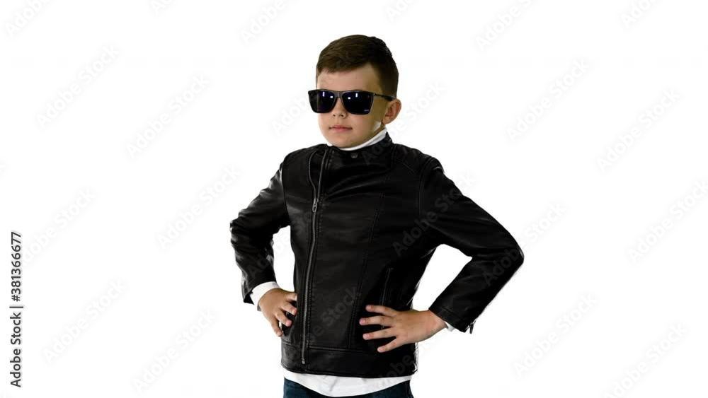 Young boy in a leather jacket putting on black glasses with arms on his hips on white background. Young boy in a leather jacket putting on black glasses with arms on his hips on white background.