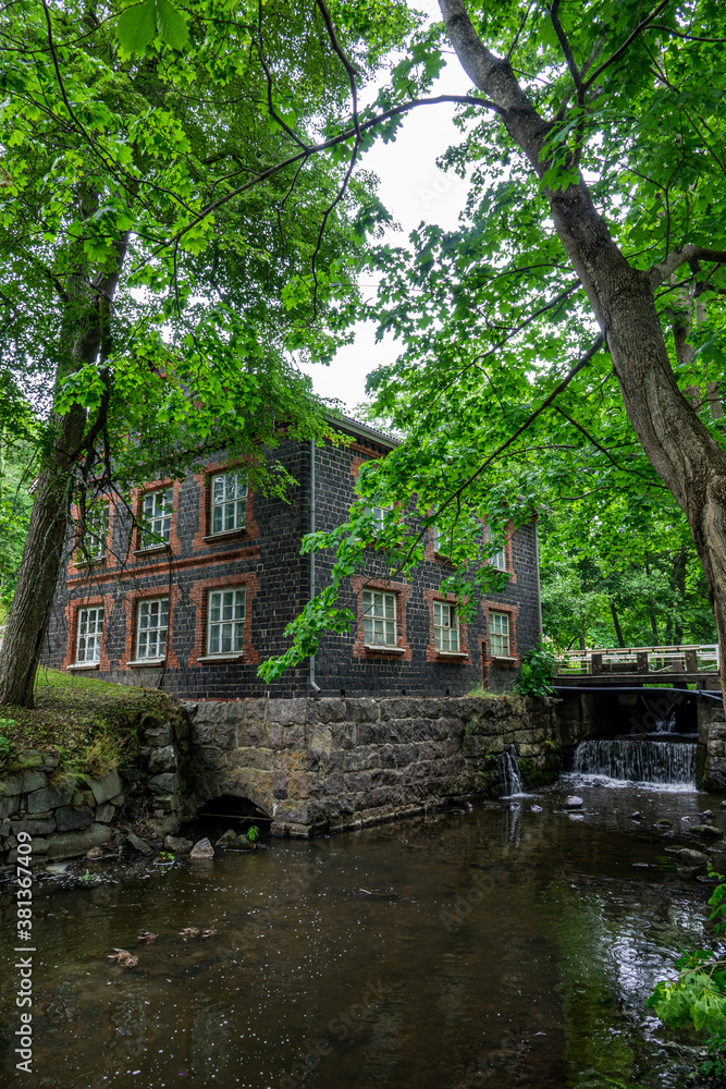 Fiskars village and its mill in the summer time. Former iron works mill built of slag brick (built in 1898). Some trees and a river, Finland.