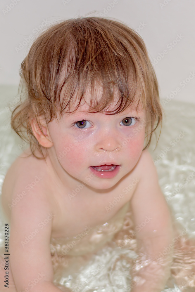 A small child bathes in the bathroom. Shot close-up, the child sits in the water and looks into the camera. A small child bathes in the bathroom. Shot close-up, the child sits in the water and looks into the camera.