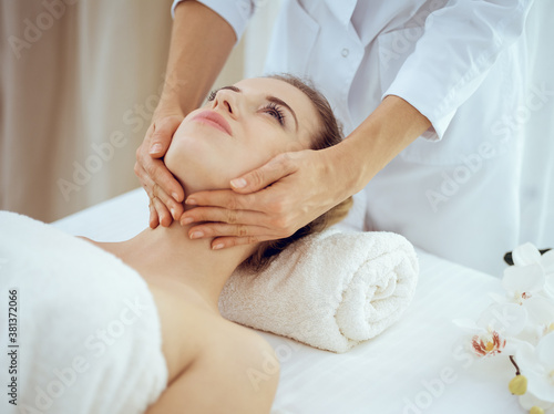 Young and blonde woman enjoying facial massage in spa salon. Beauty concept