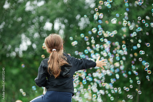 The girl is trying to catch soap bubbles. Lots of soap bubbles.