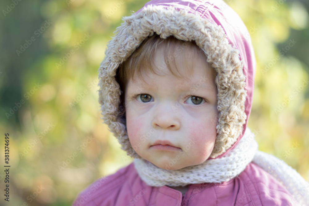 The kid in warm clothes looks sadly at the cameras. The child is wearing a pink hooded jacket and a white scarf. The kid in warm clothes looks sadly at the cameras. The child is wearing a pink hooded jacket and a white scarf.