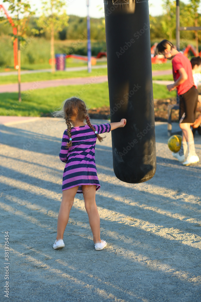 Obraz premium Back portrait of a boxing toddler girl with a punching bag on the outdoor sports ground
