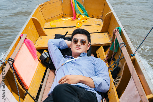 Business man wear sunglasses sleep on wooden boat in Bangkok.