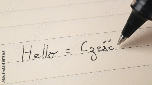 Beginner Polish language learner writing Hello word Czesc for homework on a notebook