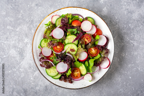 Healthy vegetable salad of cherry tomatoes, cucumber slices, green and purple lettuce leaves, onions and olive oil in plate on concrete table Top view Flat lay Diet, mediterranean menu Vegan food